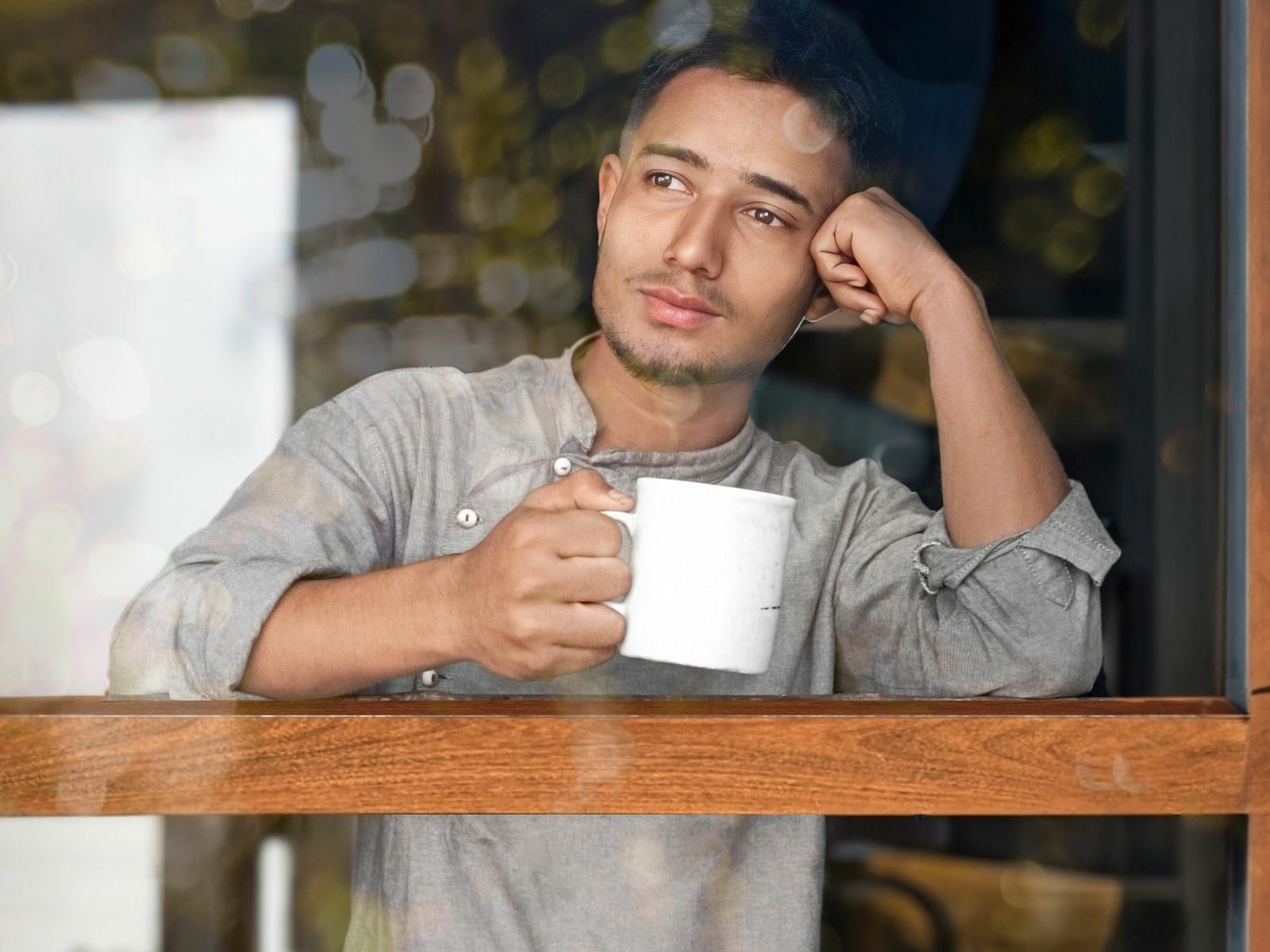 Homme tenant une tasse de café, lumière chaude derrière une vitre