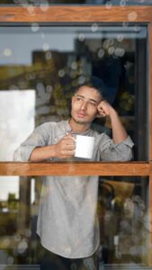 Homme tenant une tasse de café, lumière chaude derrière une vitre